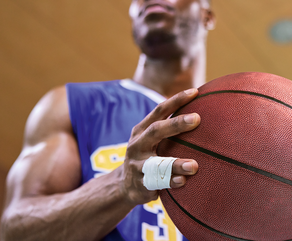 Close-up of a basketball player holding a ball, with his fingers taped for protection and support. Close-up of a basketball player holding a ball, with his fingers taped for protection and support.